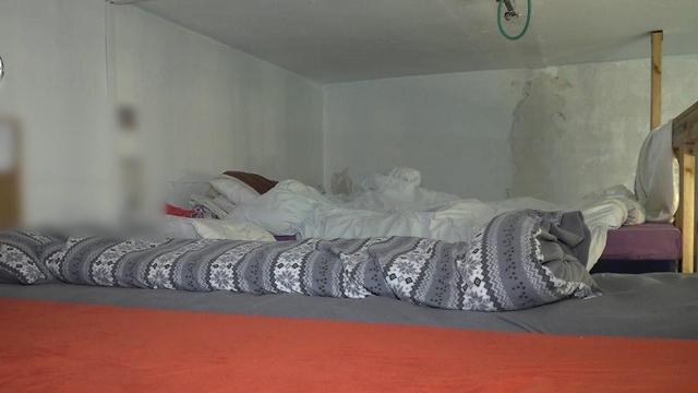 "מיטת" קומותיים, שימו לב שאין אפילו סדין על משהו שנראה כמו מזרן בצבע סגול מזוהם, שמיכות מלוכלכות, חשמל חשוף בתקרה והקירות ללא תמונה - זה חדר ילדים